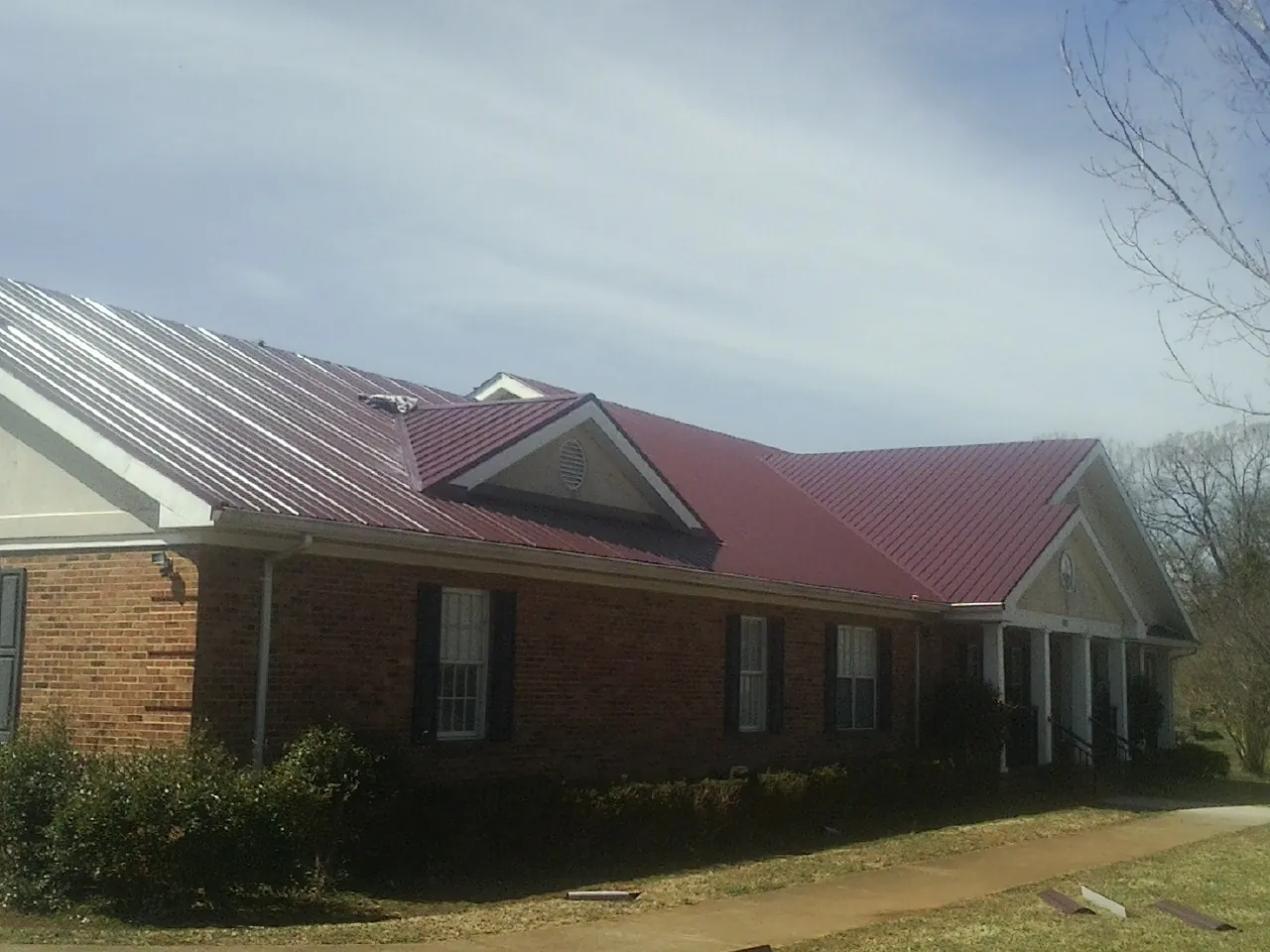 Red metal roof with gabled entries on a long brick building, from a Hail Damage Roof Repair job in Palermo