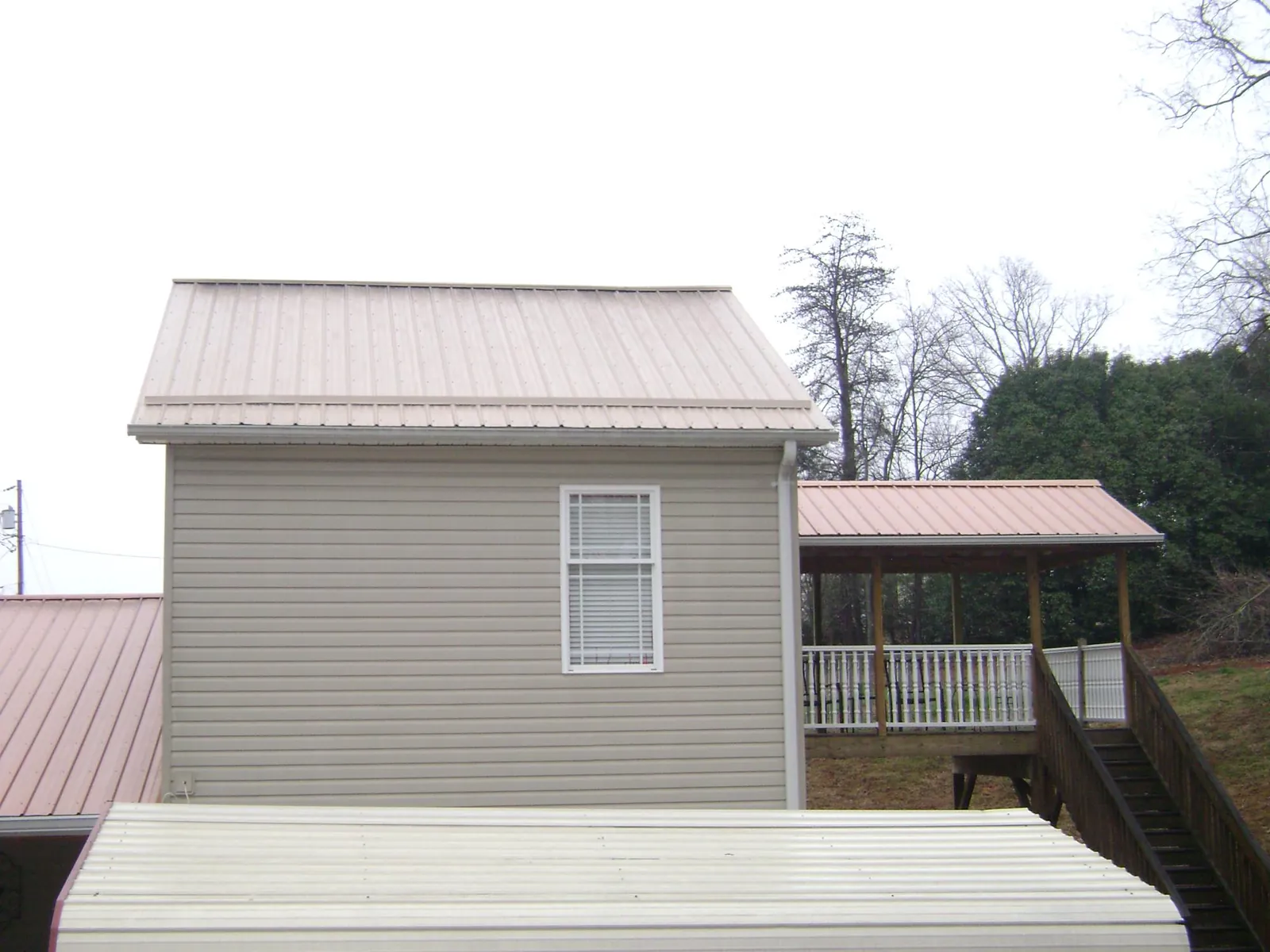 Tan metal roofs on a two story addition and attached porch, from a Roof Replacement job in Palermo